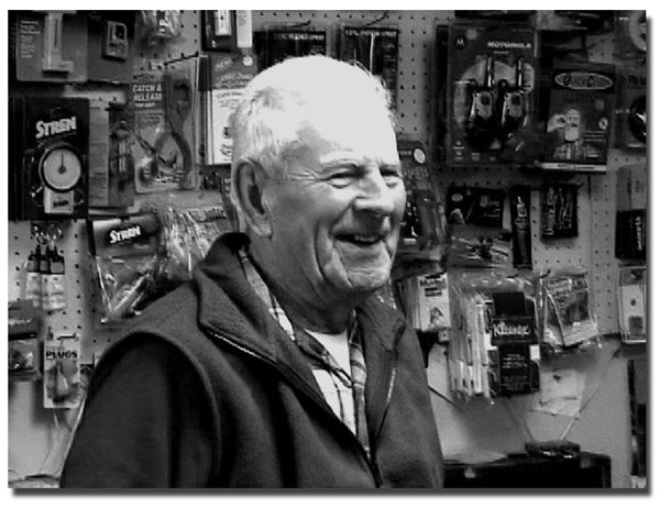Bill Martel laughing in the store surrounded by fishing lures and gadgets.